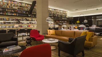 A modern library with bookshelves, a leather sofa, and red chairs.