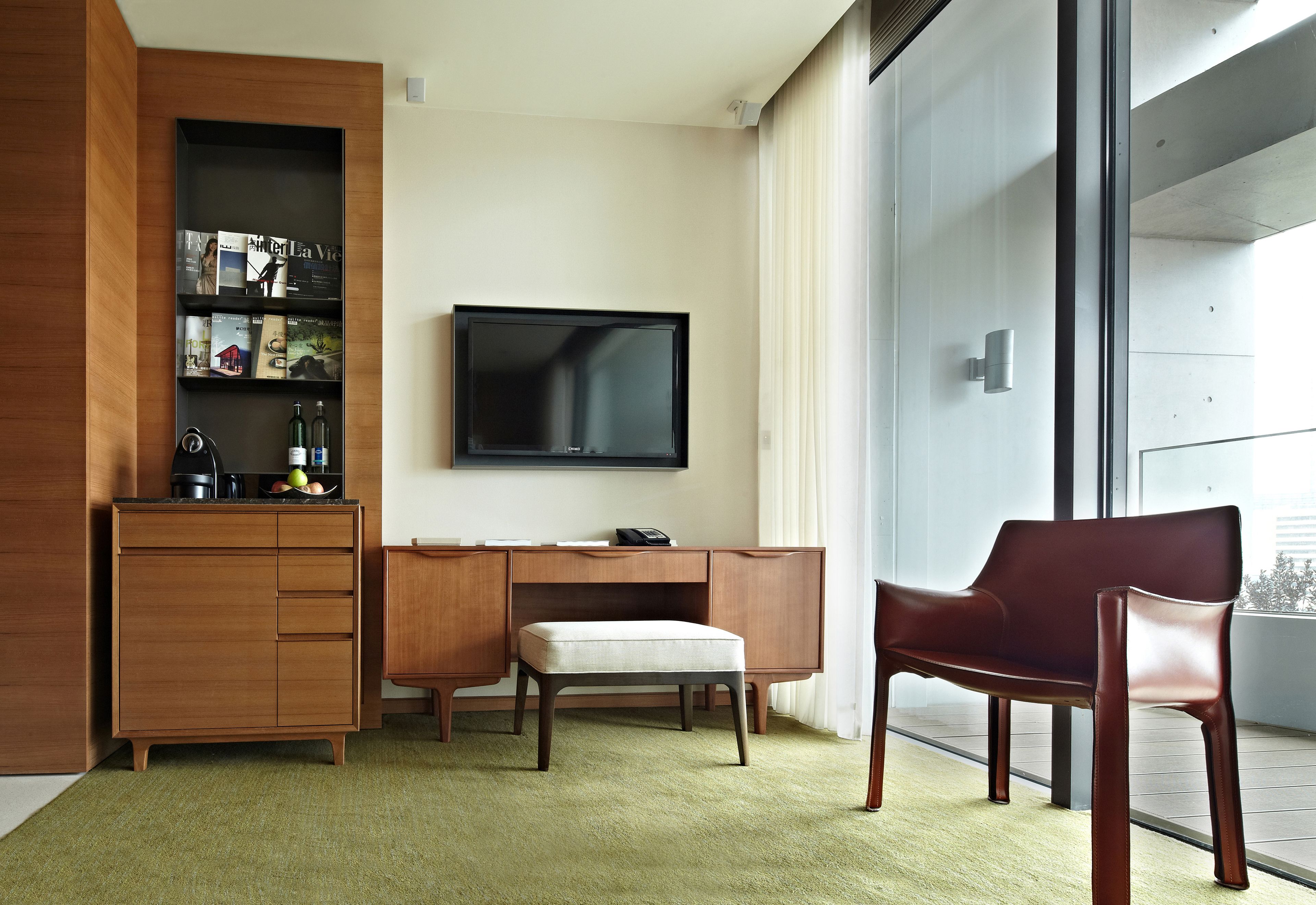 A modern hotel room with a wooden cabinet, a desk, a television, and a red chair.