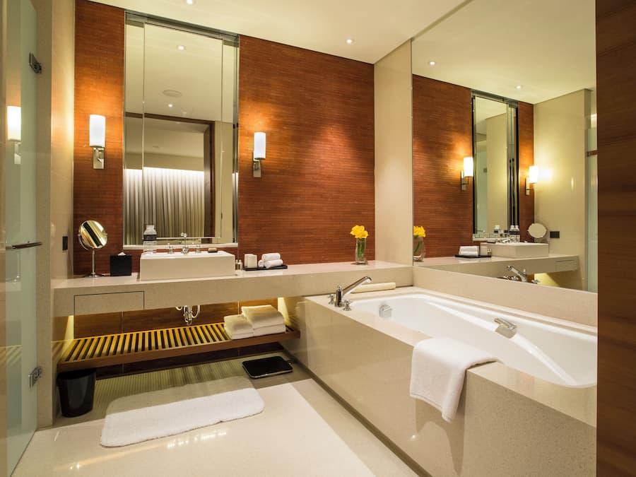 A modern bathroom with a large bathtub, a sink, and a mirror. There are towels and toiletries on the counter.