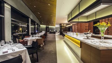 A modern restaurant with a long counter, multiple tables, and a brick wall backdrop.
