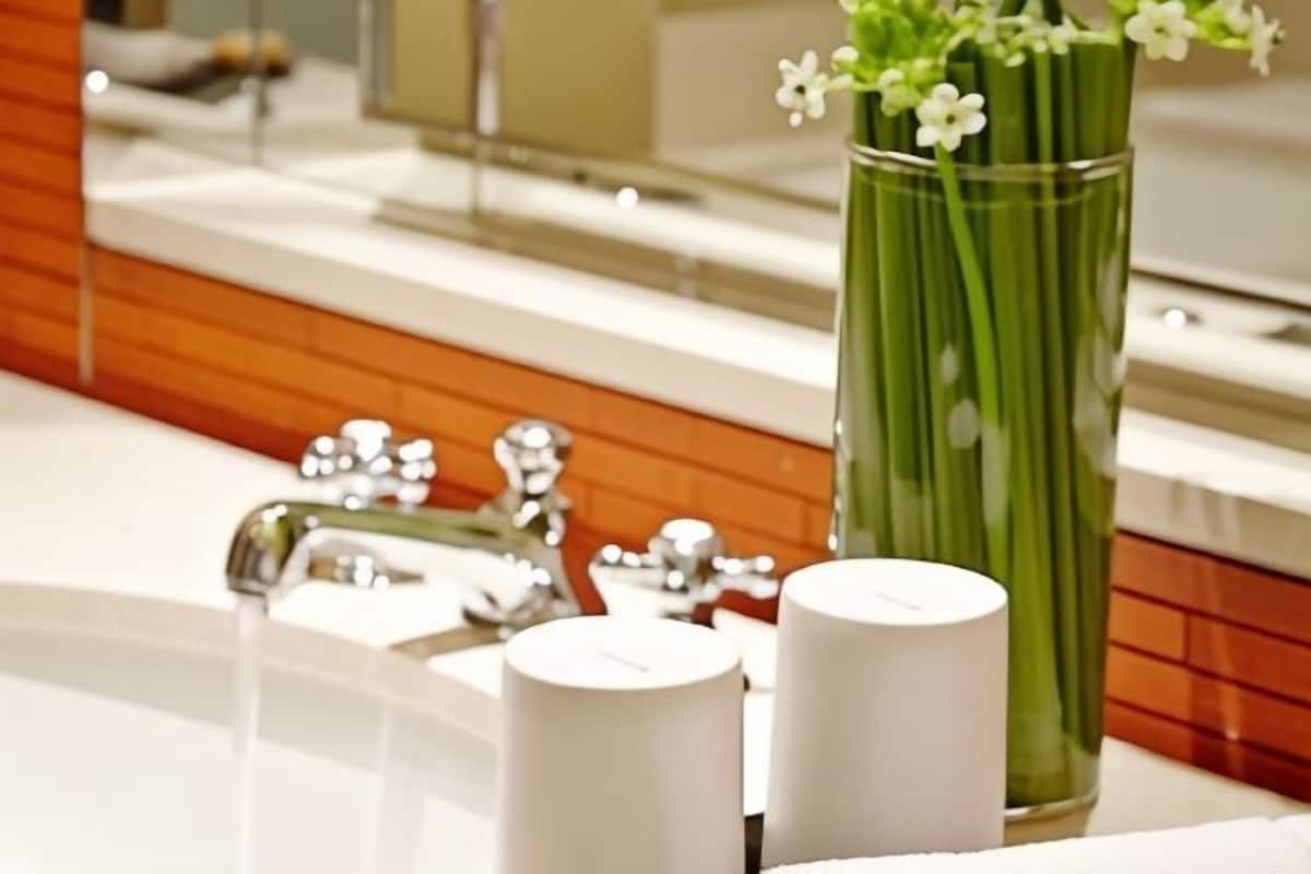 Une salle de bain avec un miroir, un lavabo et un vase rempli de fleurs.