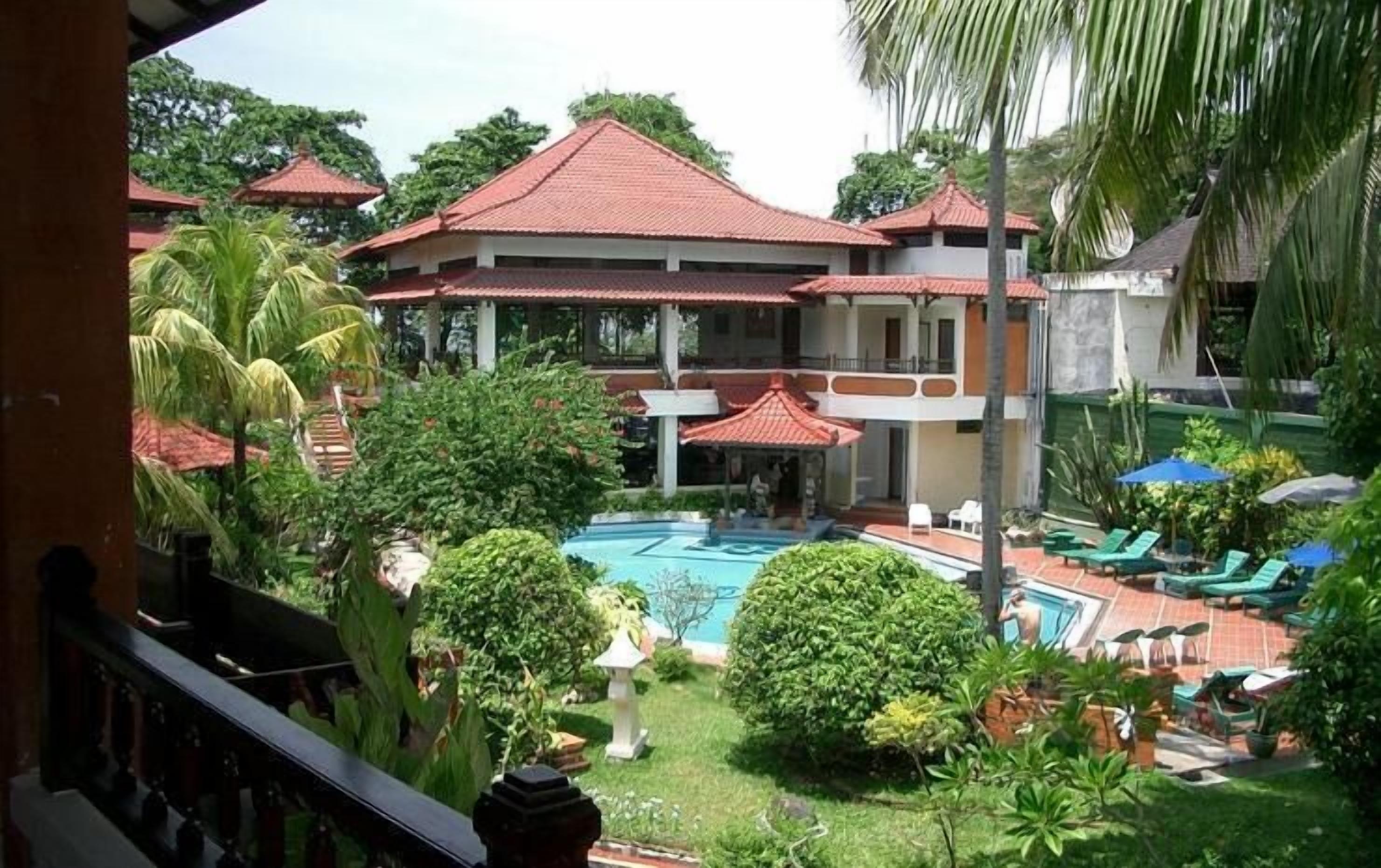 A hotel with a swimming pool surrounded by lush greenery and palm trees.