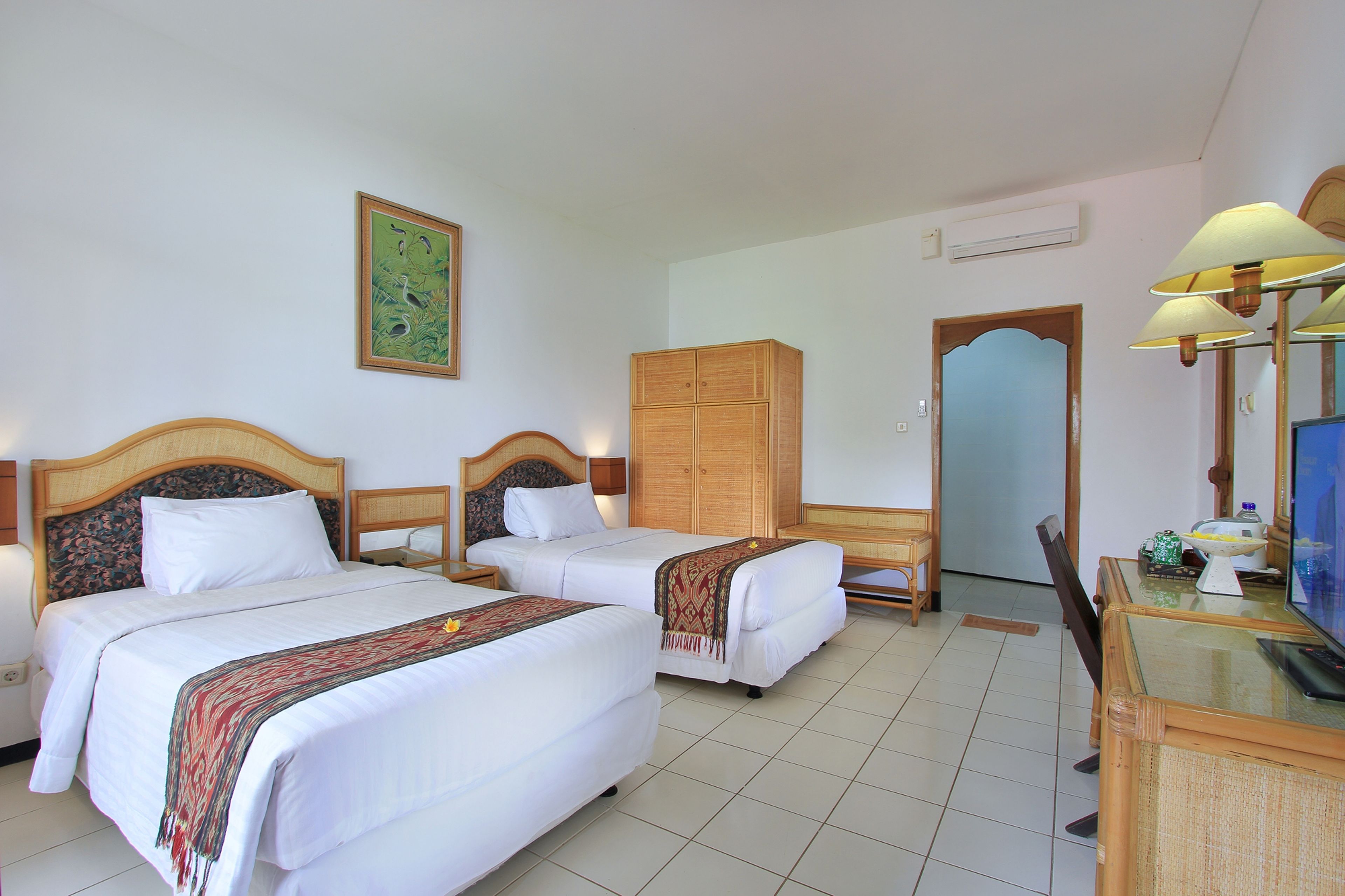 A hotel room with two beds, a wooden wardrobe, a television, and a dining table.