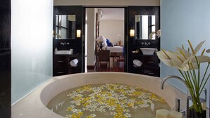 A bathroom with a large bathtub filled with water and floating flowers, a sink, and a mirror. - Temple Hill Residence Villa (Jimbaran)