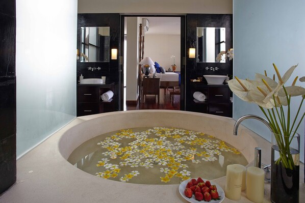 Un baño con una bañera grande llena de agua y flores flotando, un lavamanos y un espejo.