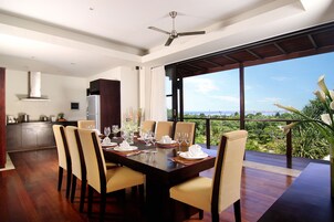 Comedor con una mesa grande dispuesta para seis personas, cocina al fondo y balcón con vistas al exterior.