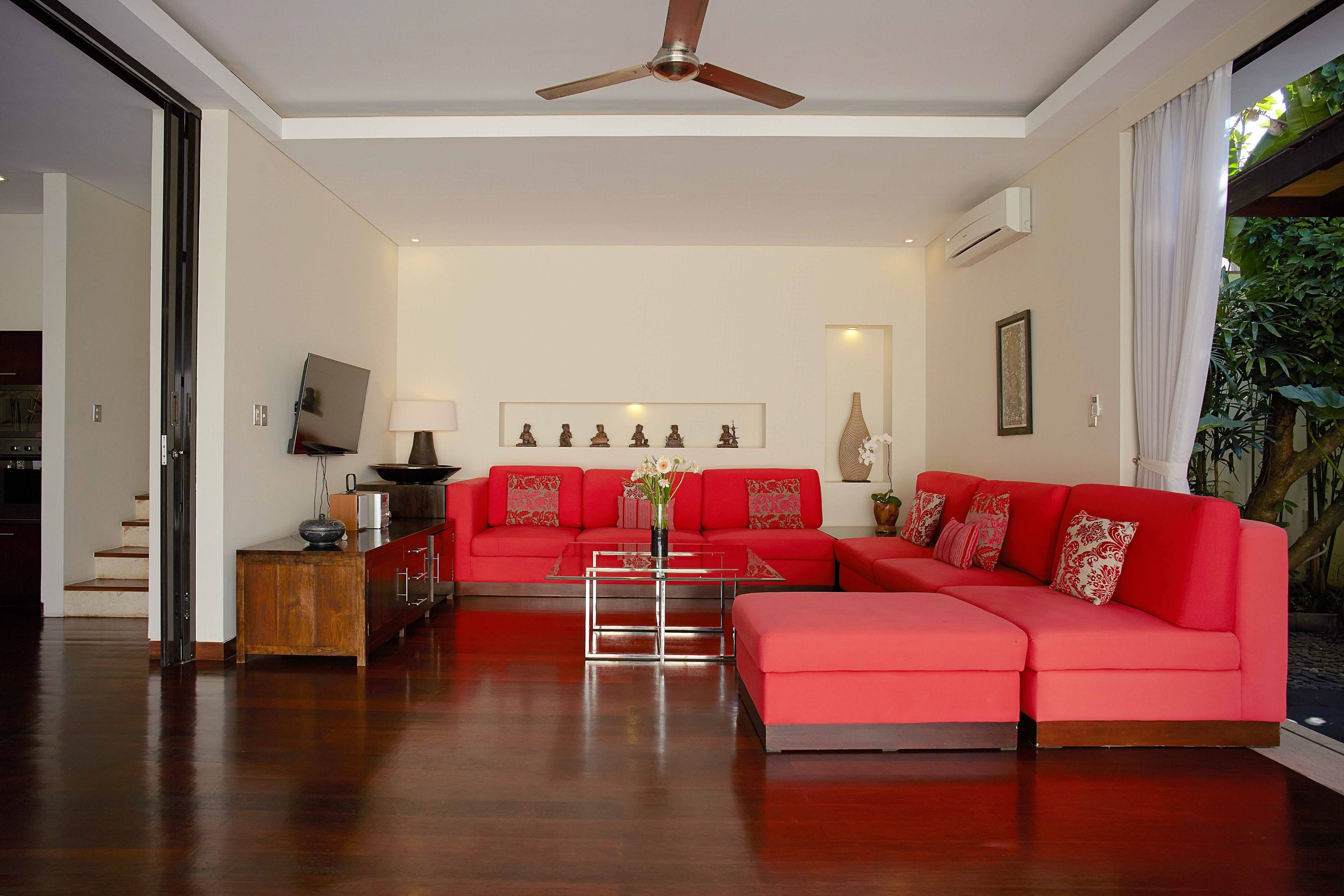 A modern living room with a red sofa, a glass coffee table, and a ceiling fan.