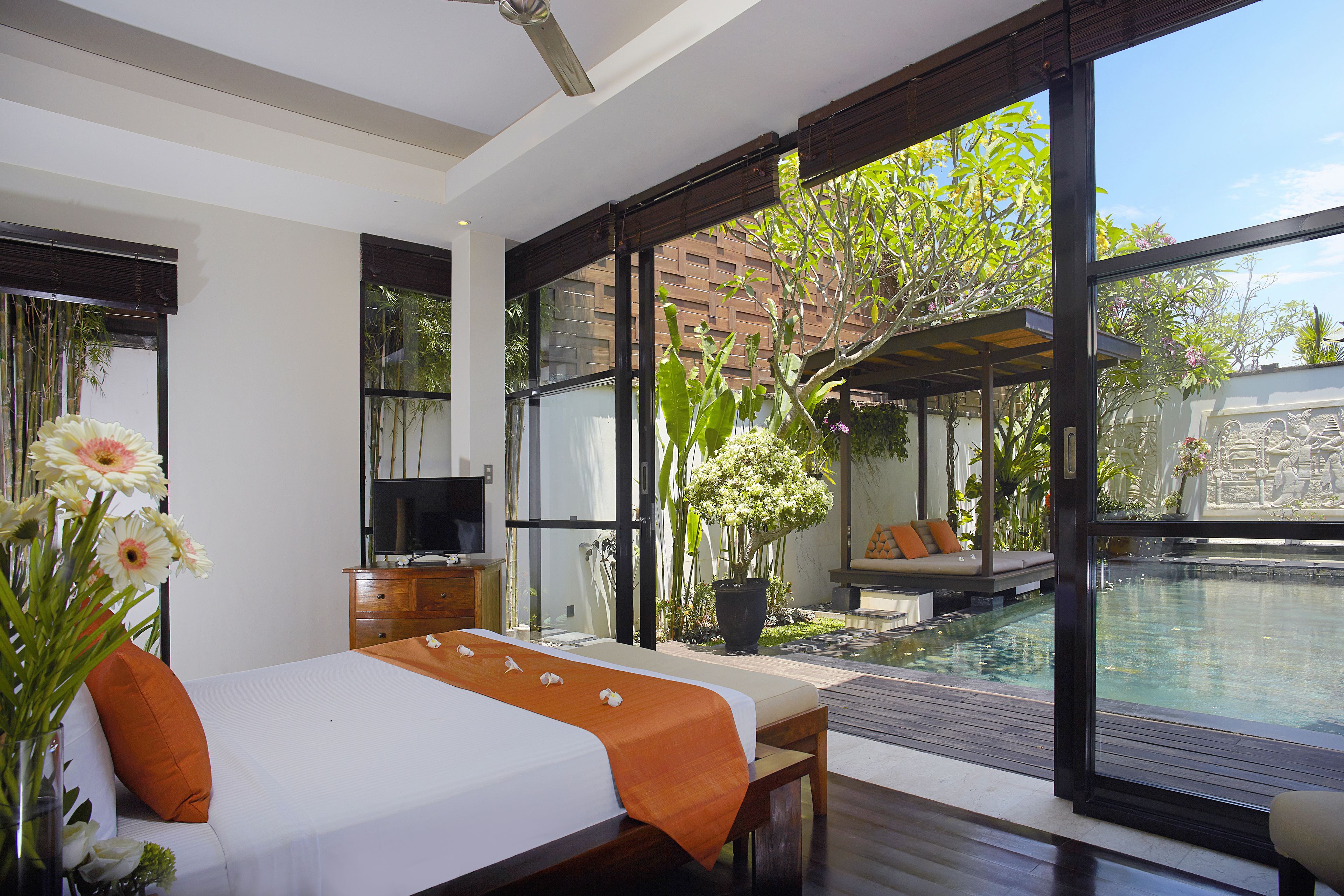 A modern bedroom with a large bed, a TV, and a view of an outdoor swimming pool.