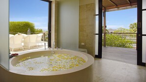 A modern bathroom with a large bathtub filled with flower petals, a toilet, and a shower area. - Temple Hill Residence Villa (Jimbaran)