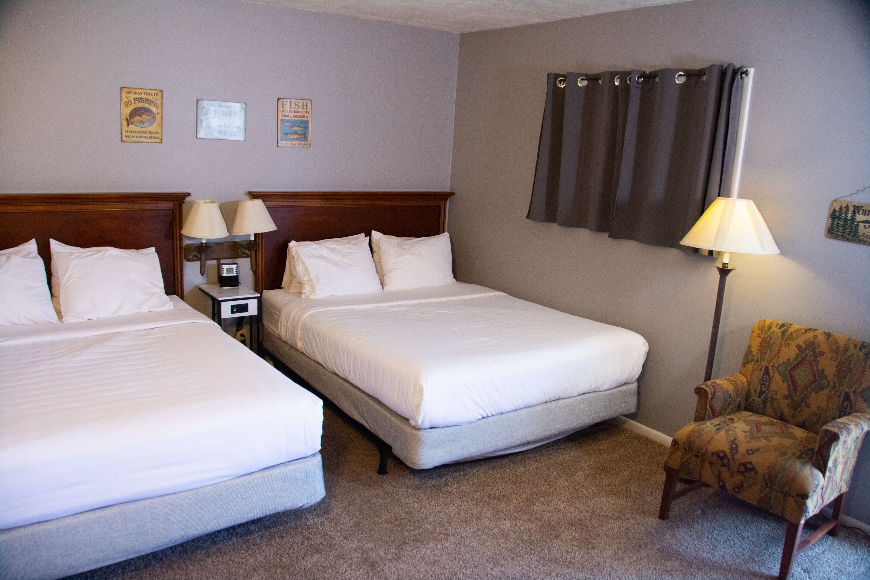 A hotel room with two single beds, a nightstand with lamps, a chair, and a curtain.
