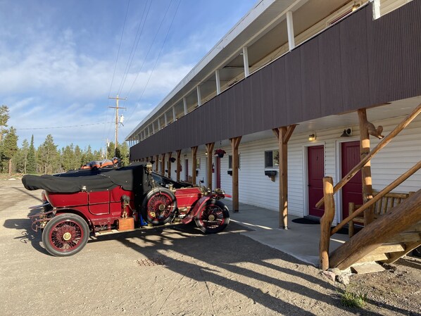 Guests can park their vehicle on the gravel surface in front of this building with a flat roof and wooden porch.