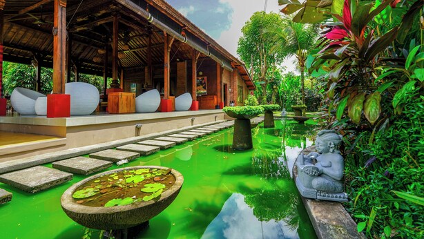 A traditional wooden structure with a covered walkway, a stone water feature with lily pads, and a statue of a seated figure. - Ubud Heaven Penestanan (Ubud)
