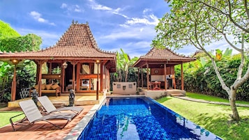 Un área de piscina con dos gazebos de madera, una tumbona y una estatua.