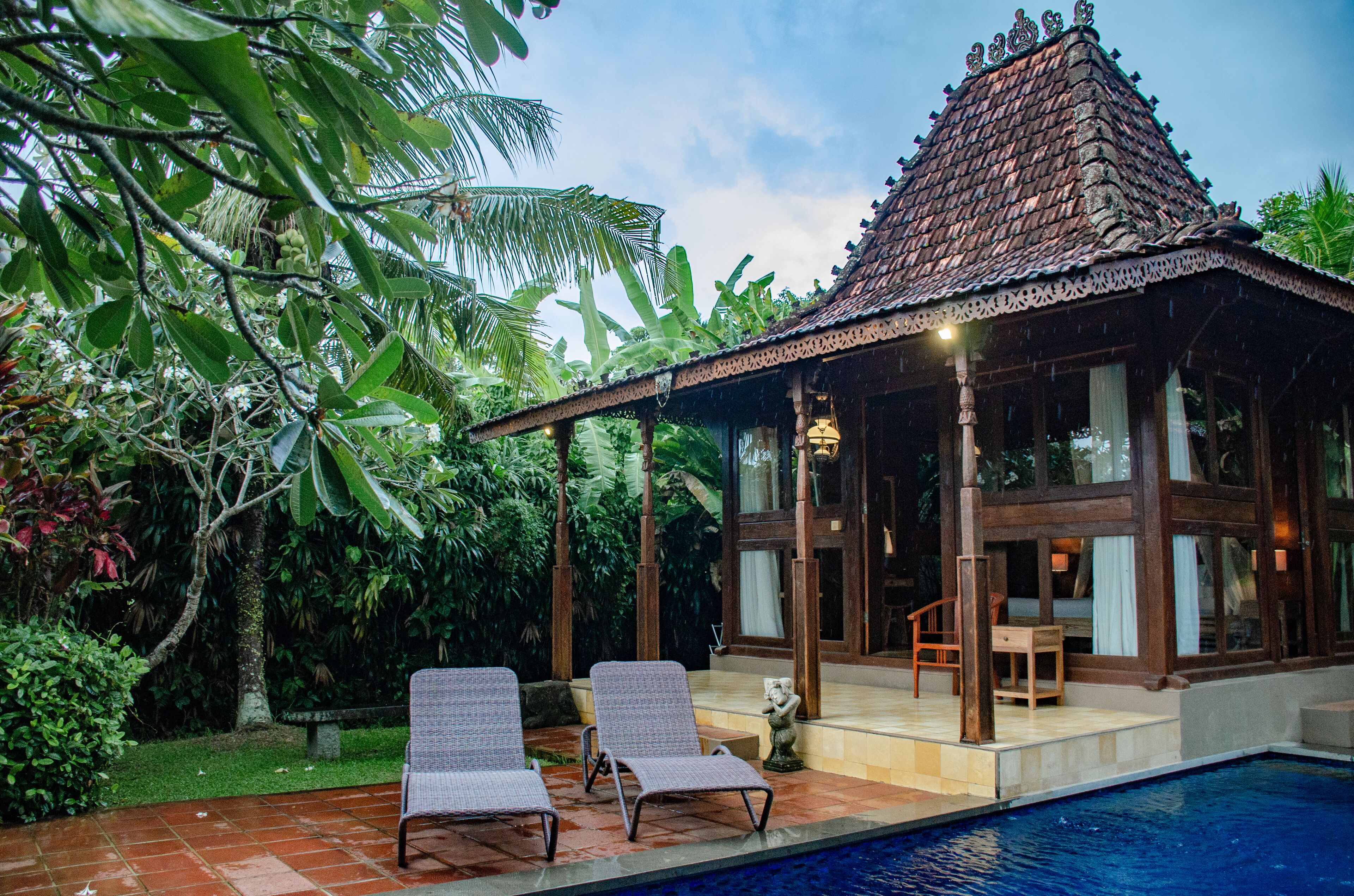 A traditional house with a tiled roof and a pool area with two lounge chairs.