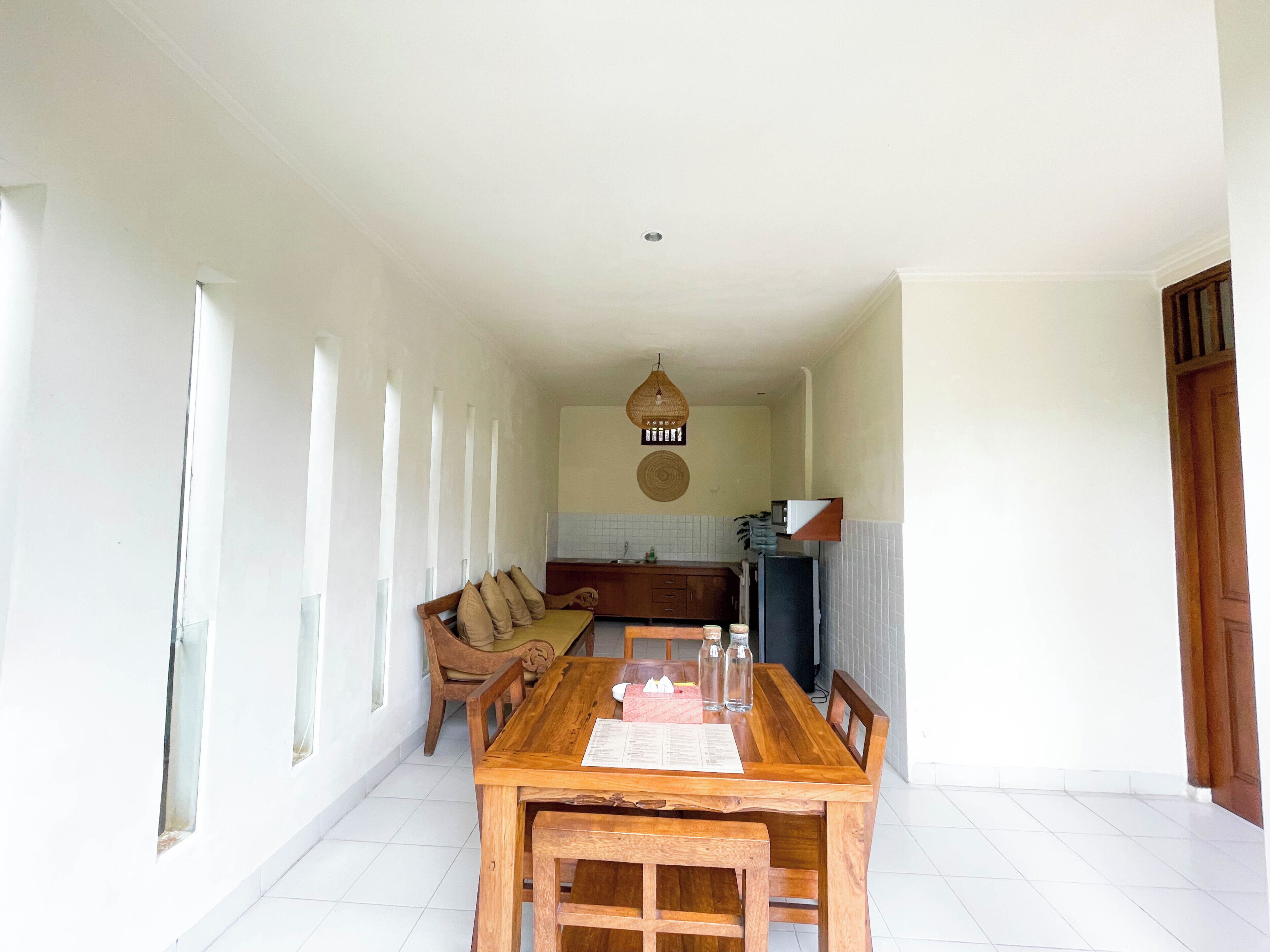 Un vaste espace dédié à la salle à manger, avec une table et des bancs en bois, une cuisine à l’arrière-plan et une grande fenêtre qui laisse entrer la lumière naturelle.