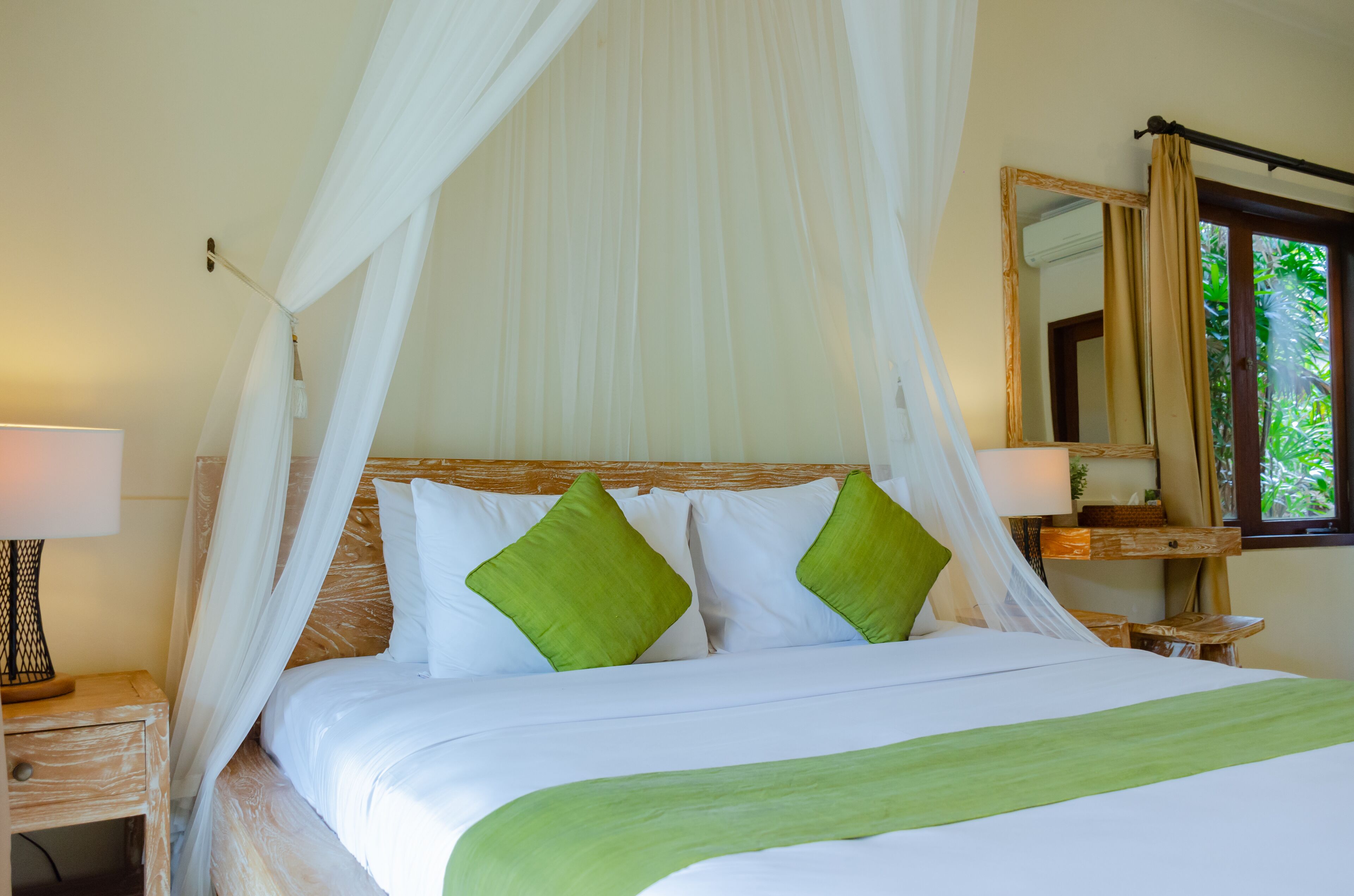 A bed with white bedding and green pillows, a wooden headboard, a nightstand with a lamp, and a mirror on the wall.