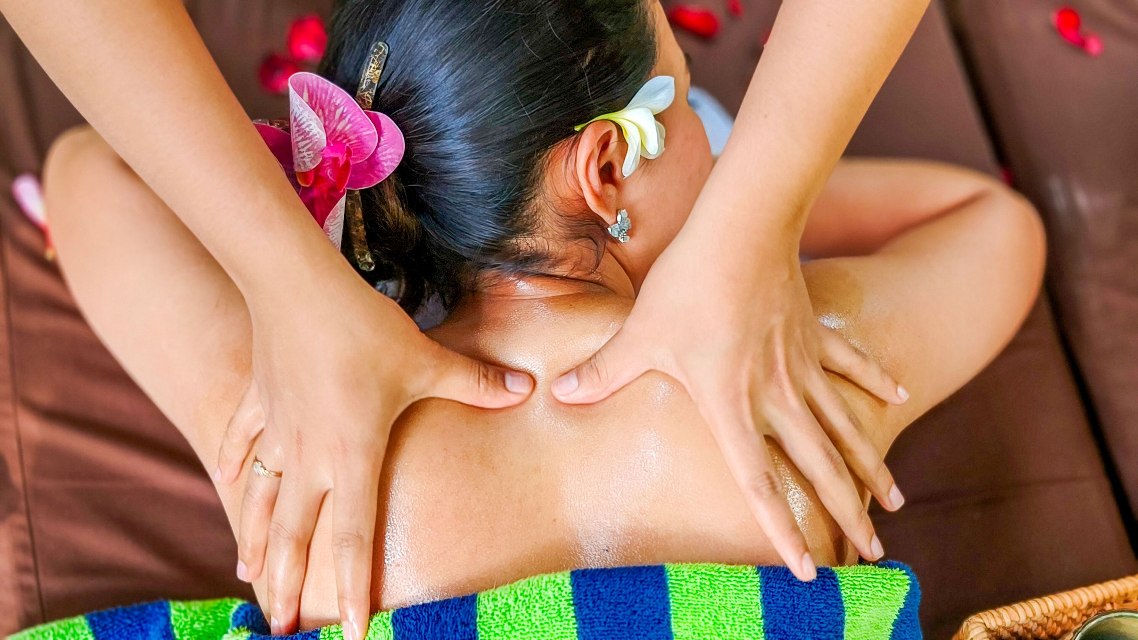A person receiving a back massage on a brown couch with a patterned towel.