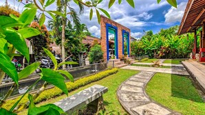 A courtyard with a stone pathway, a bench, and a building with blue columns. - Ubud Heaven Penestanan (Ubud)