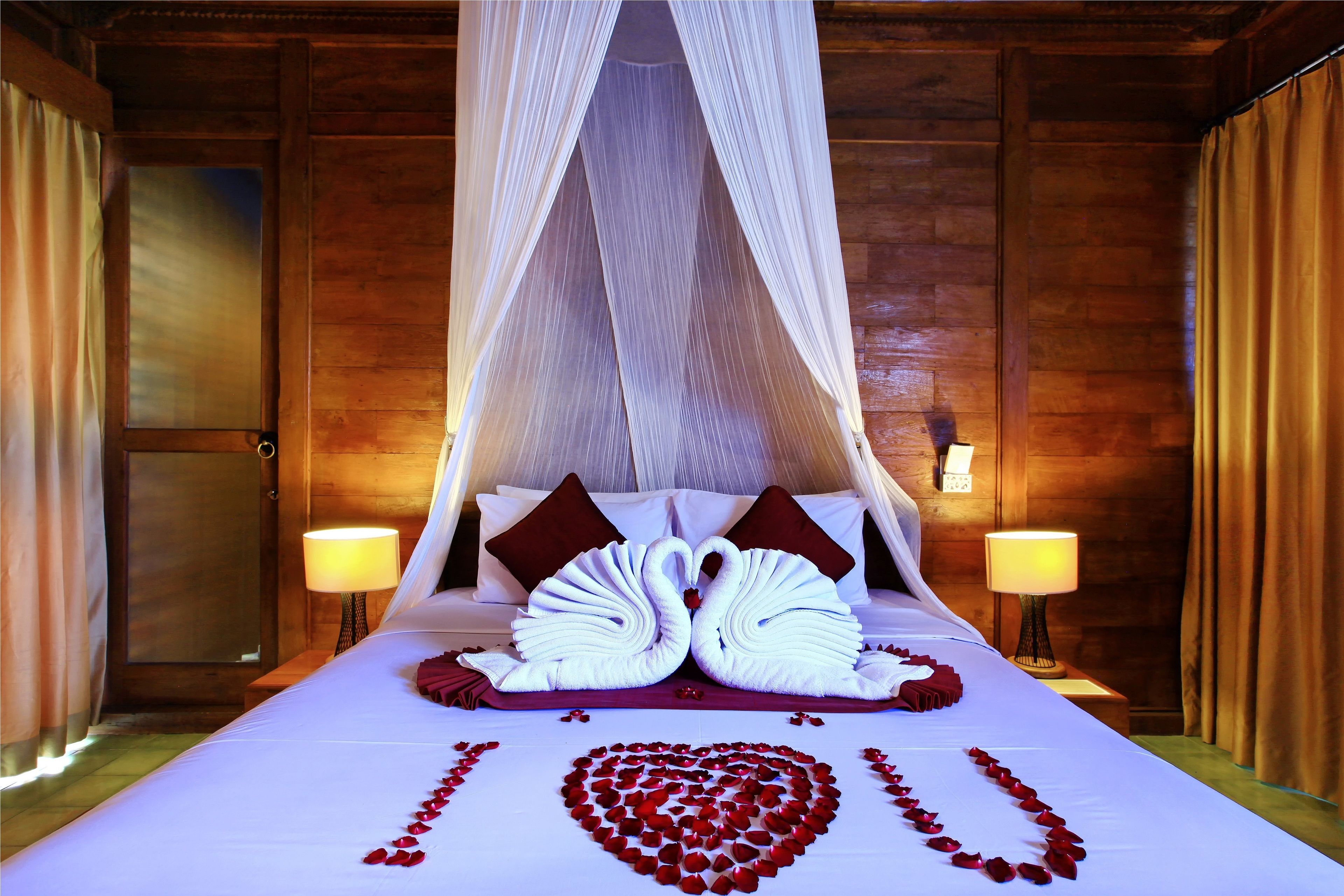 A neatly made bed with a heart-shaped arrangement of rose petals and two swan-shaped towels.