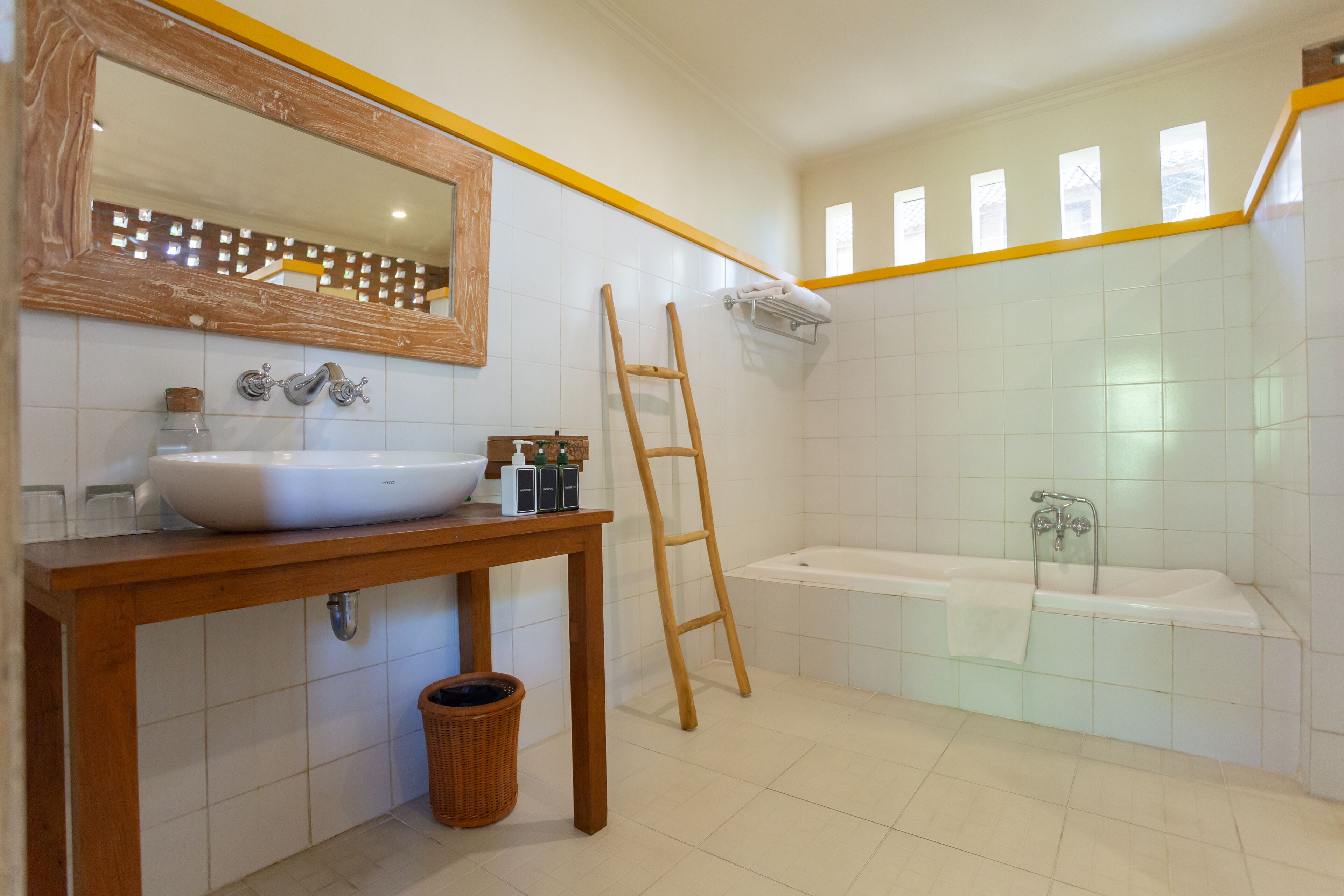 A bathroom with a wooden vanity, a large mirror, a bathtub, and a wooden ladder.