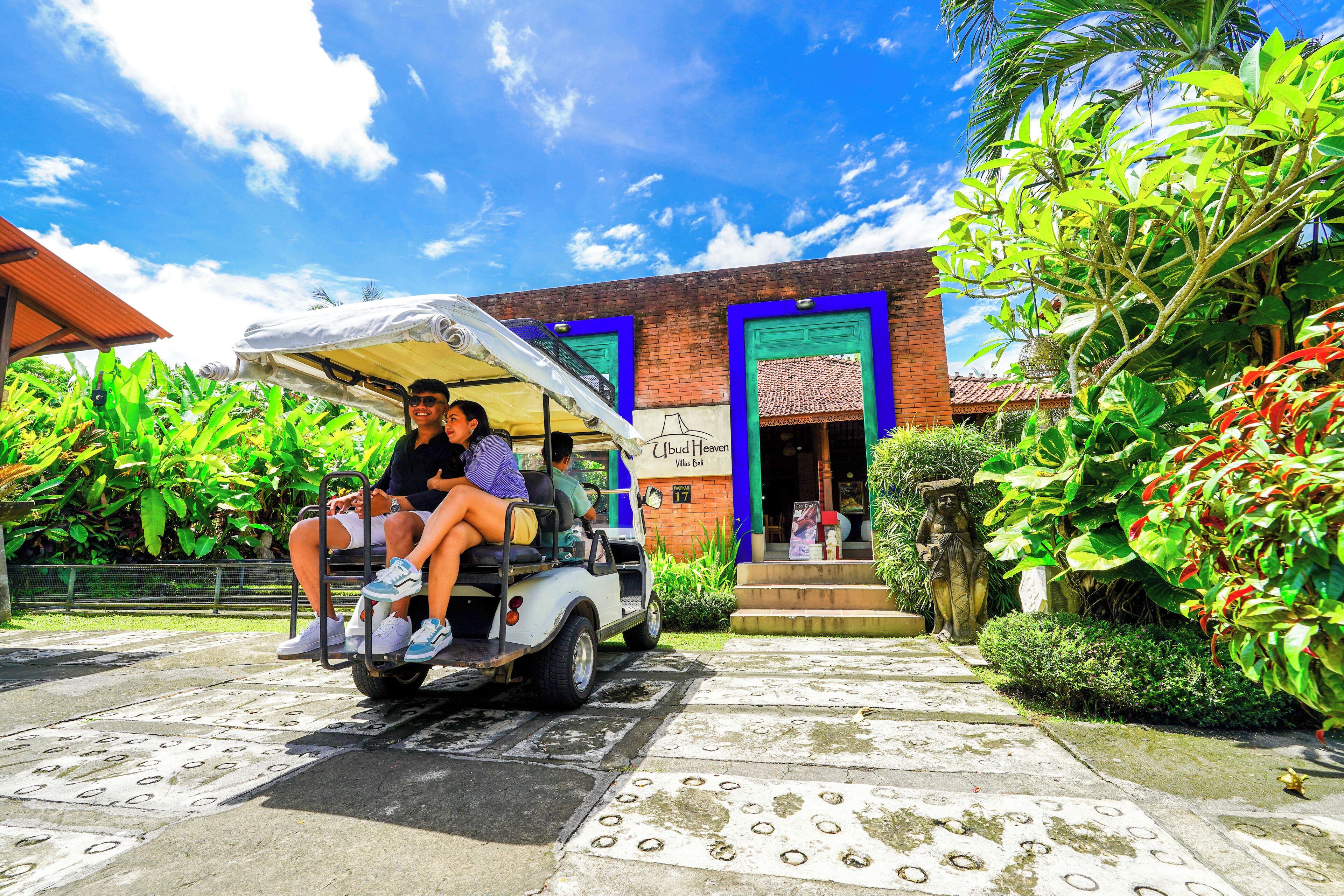 Un carrito de golf blanco con pasajeros, estacionado frente a un edificio con puerta azul y un letrero que dice 'Villa Bella'.