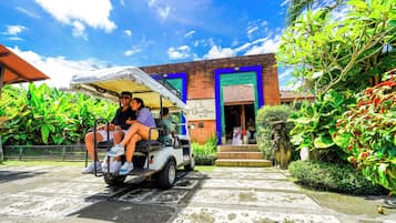 Un carrito de golf blanco con pasajeros, estacionado frente a un edificio con puerta azul y un letrero que dice 'Villa Bella'.