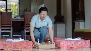 A person arranging a tray with toiletries on a bed in a room with wooden furniture and a window with a view of greenery. - Ubud Heaven Penestanan (Ubud)
