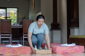 A person arranging a tray with toiletries on a bed in a room with wooden furniture and a window with a view of greenery. - Ubud Heaven Penestanan (Ubud)
