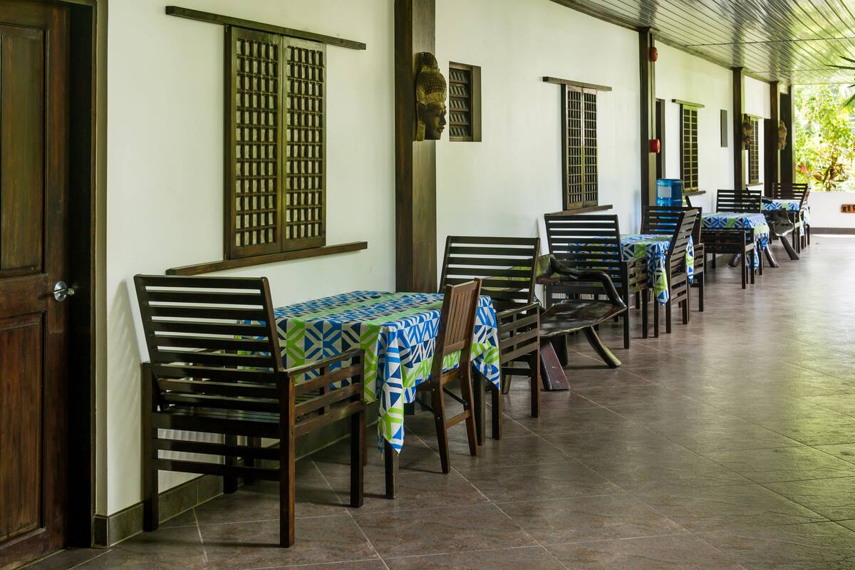 A covered outdoor seating area with wooden benches and tables, each covered with patterned tablecloths.