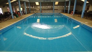 En inomhuspool med klart vatten, ett kaklat golv och en livräddarstol.