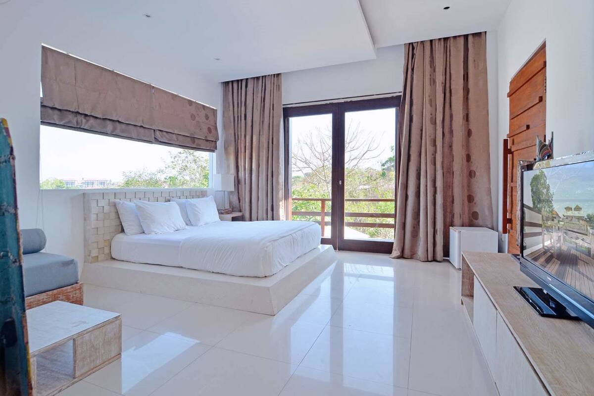 A modern bedroom with a large bed, a TV, and a balcony with curtains.