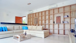 A modern living room with a beige sofa, blue cushions, a coffee table, and a wooden bookshelf. - Scene Estate (Nusa Dua)