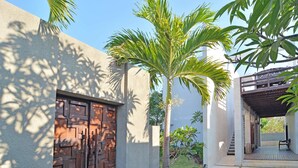 A modern building with a wooden gate, a covered patio area, and a palm tree. - Scene Estate (Nusa Dua)