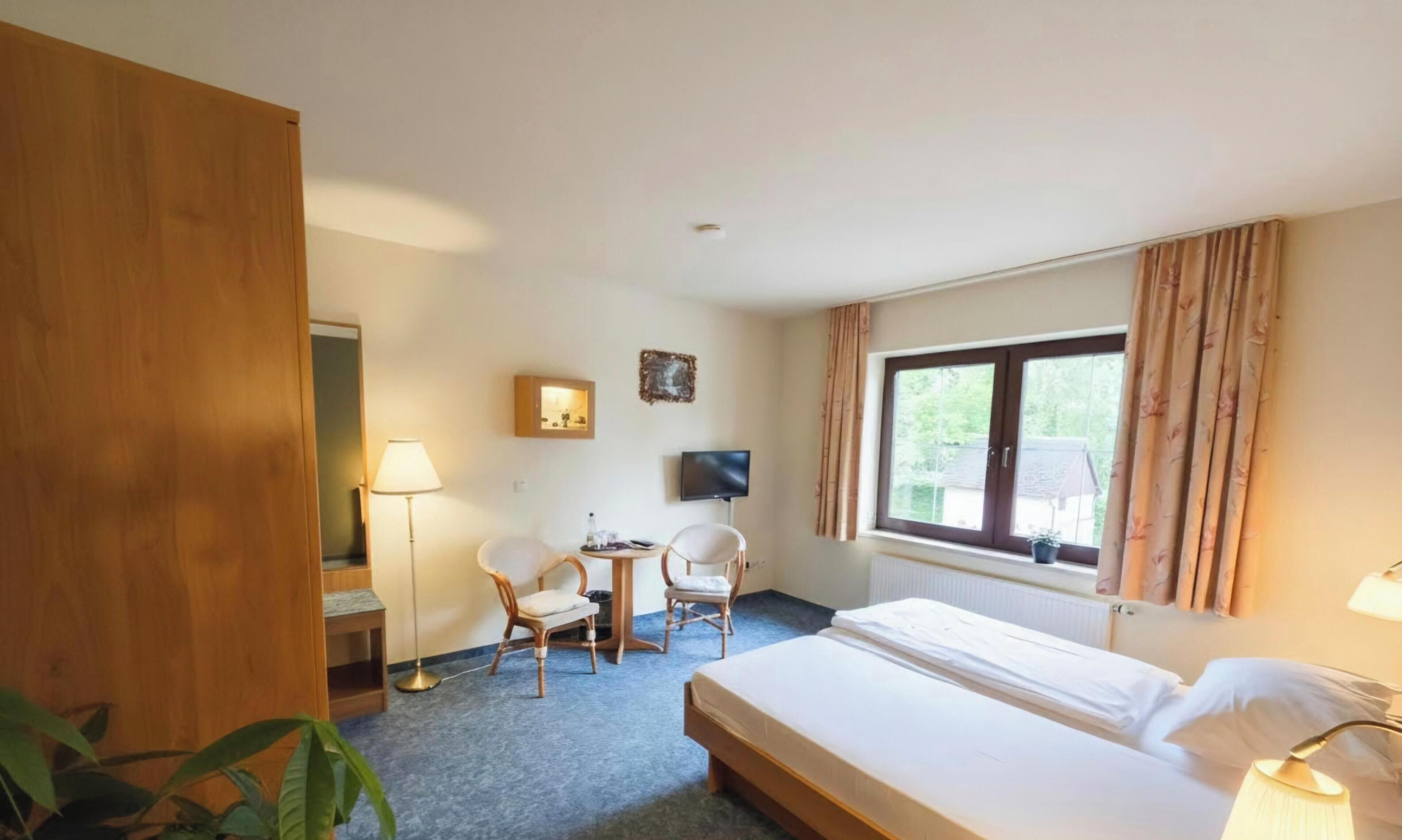 Una habitación de hotel con una cama, dos sillas, un escritorio, un televisor y una ventana con cortinas.
