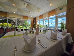 A restaurant with tables set for dining, large windows with a view, and a ceiling with draped fabric. - Hotel Waldesruh (Lengefeld)