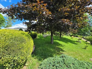 A well-maintained garden with neatly trimmed hedges, a variety of trees, and a clear sky. - Hotel Waldesruh (Lengefeld)