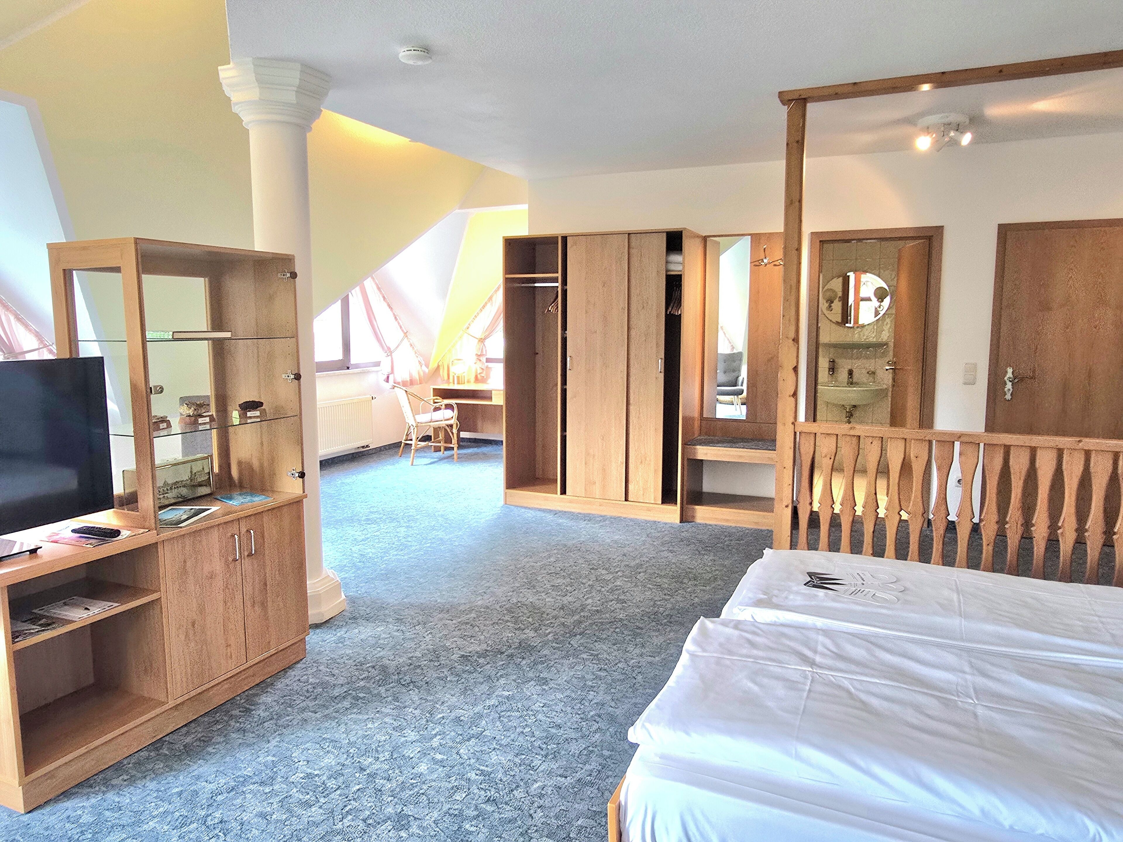 Ein Schlafzimmer mit Bett, Fernseher, Schreibtisch und Kleiderschrank.