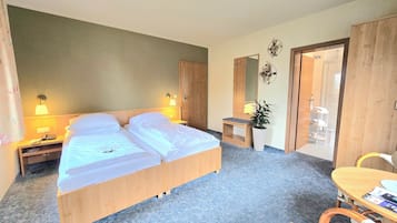 A hotel room with a double bed, bedside lamps, a small desk, a chair, and a mirror.