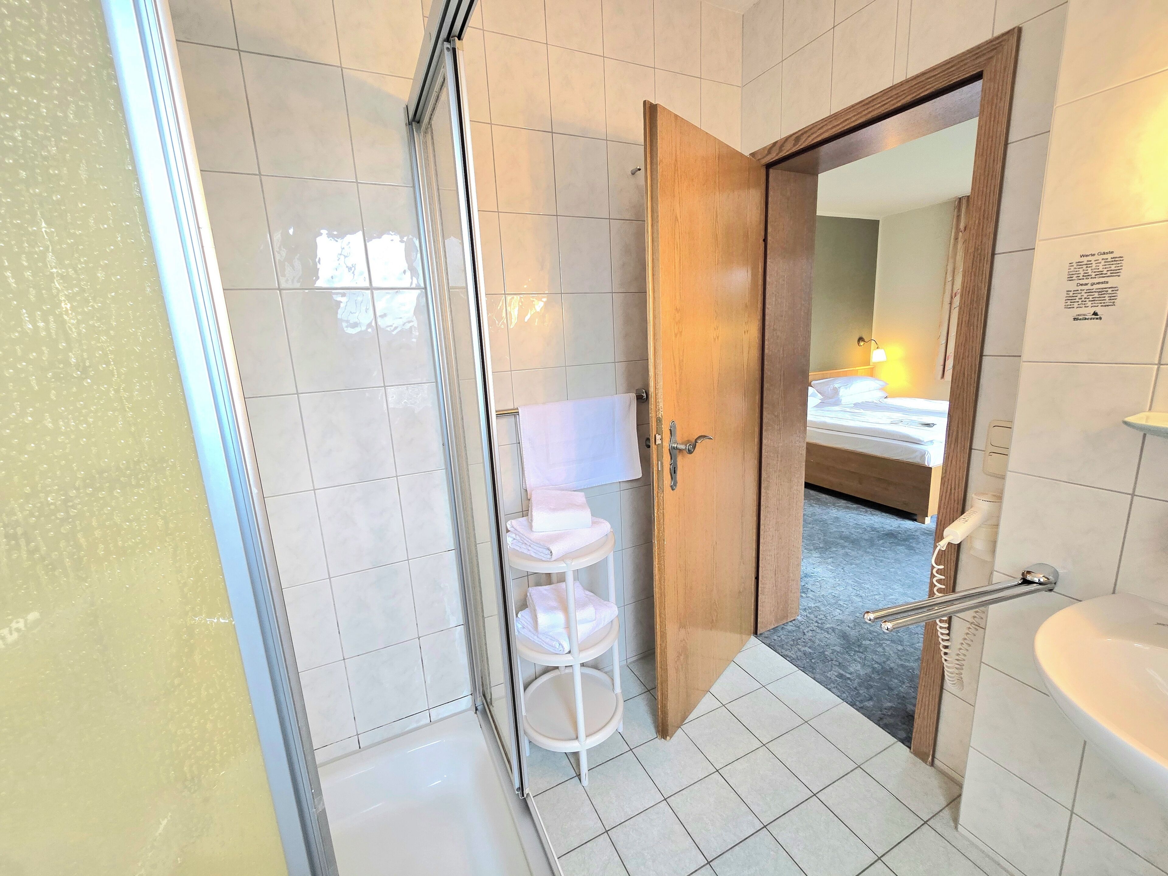 A bathroom with a shower, a sink, and a wooden door leading to a bedroom.