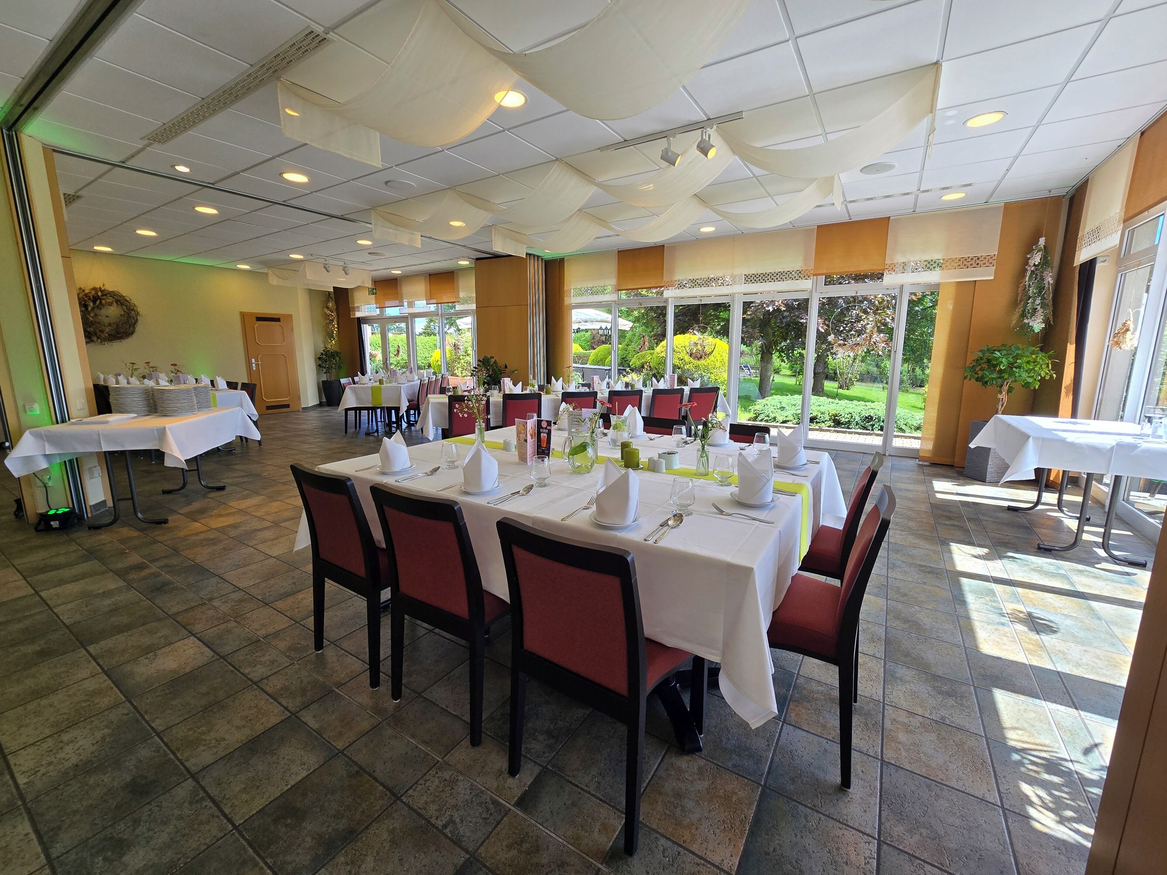 Un restaurant avec des tables dressées pour le service, des chaises et une vue sur l’extérieur.