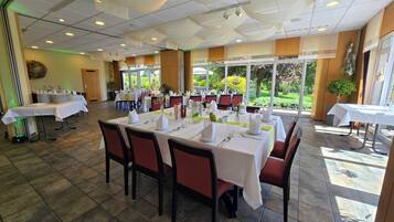Un restaurant avec des tables dressées pour le service, des chaises et une vue sur l’extérieur.