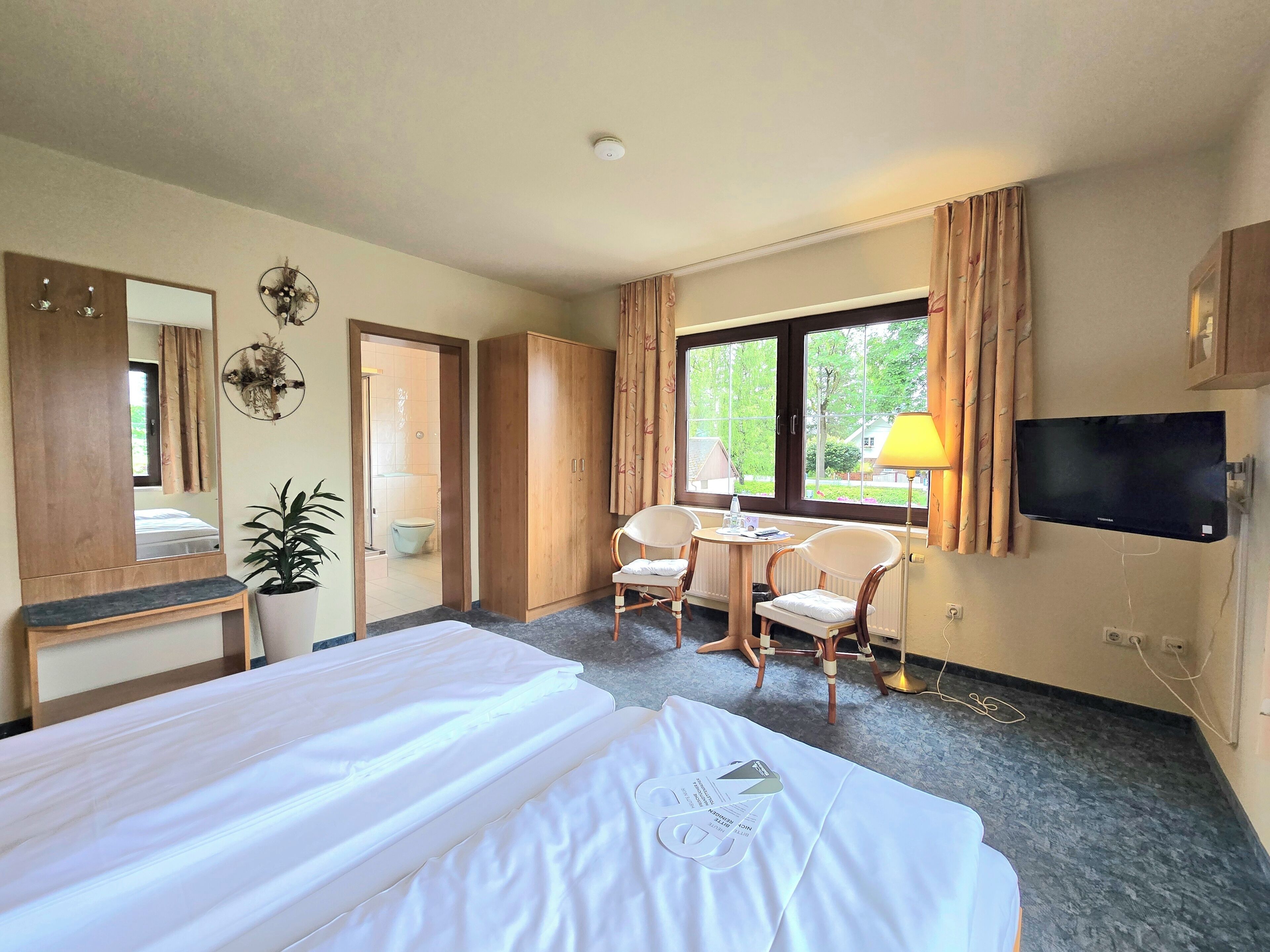 Una habitación de hotel con cama, escritorio, dos sillas, televisor y ventana con cortinas.