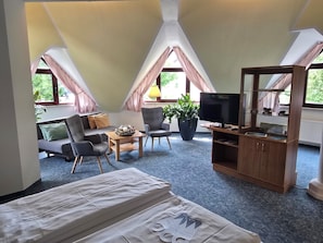 Una habitación con una cama, televisión, sofá, sillón, mesa y una planta en maceta.