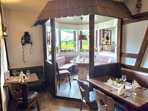 A restaurant with wooden furniture, a bay window, and a bell. - Hotel Waldesruh (Lengefeld)