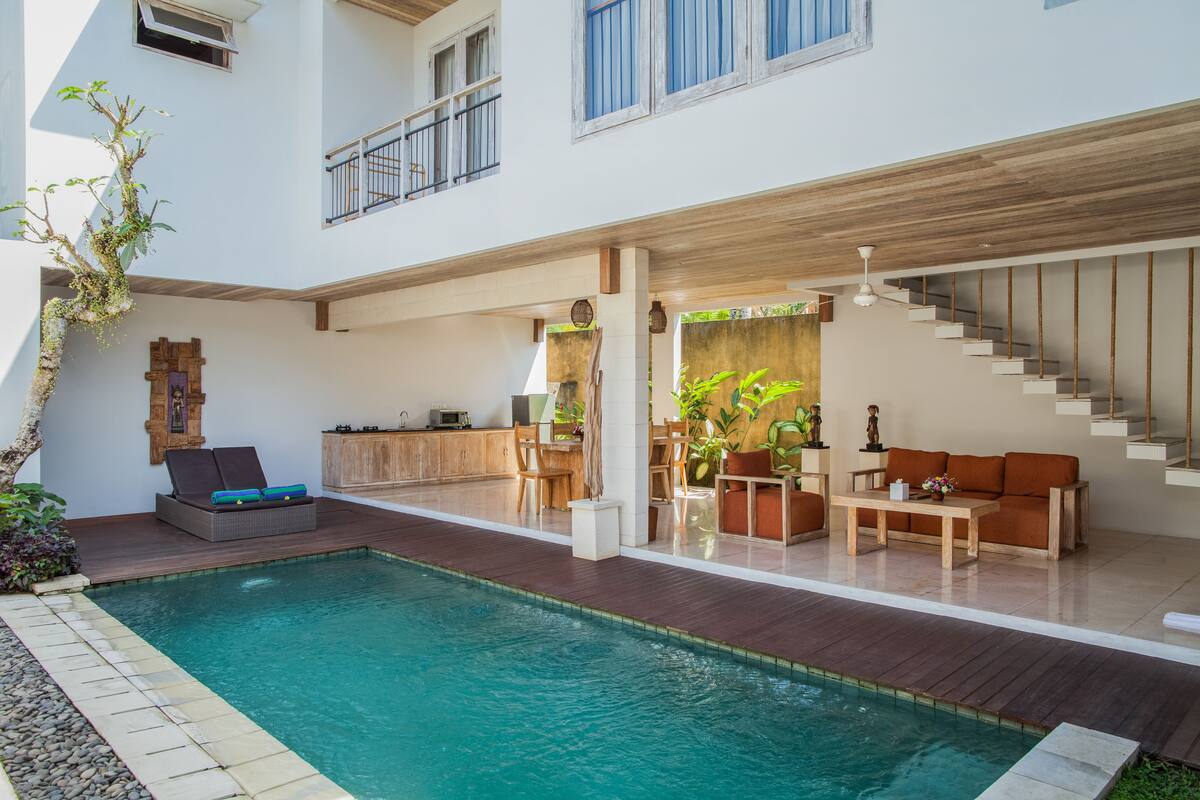 A modern indoor pool area with a wooden deck, a sofa, and a staircase.