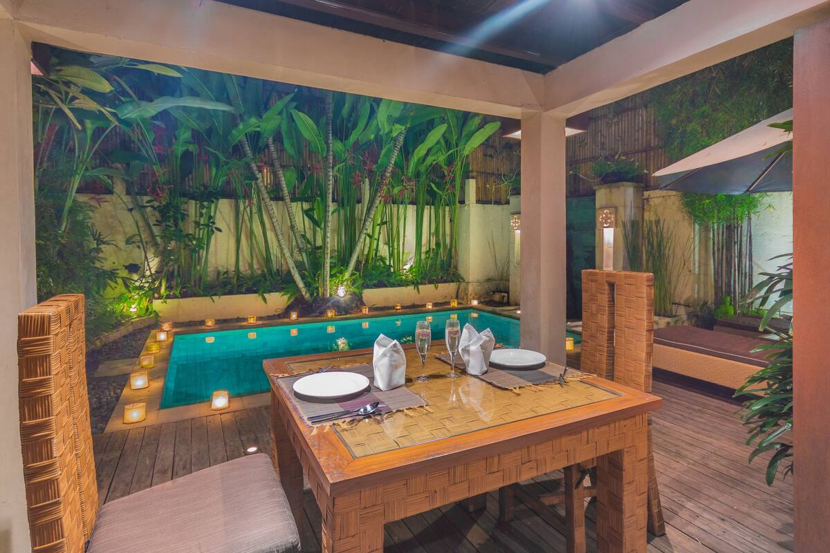Un espace extérieur aménagé pour les repas, avec une piscine, des plantes en bambou et des bougies.