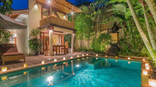 A poolside area with a wooden deck, a lounge chair, and a dining table with candles. - Villa Seriska Seminyak Bali (Seminyak)