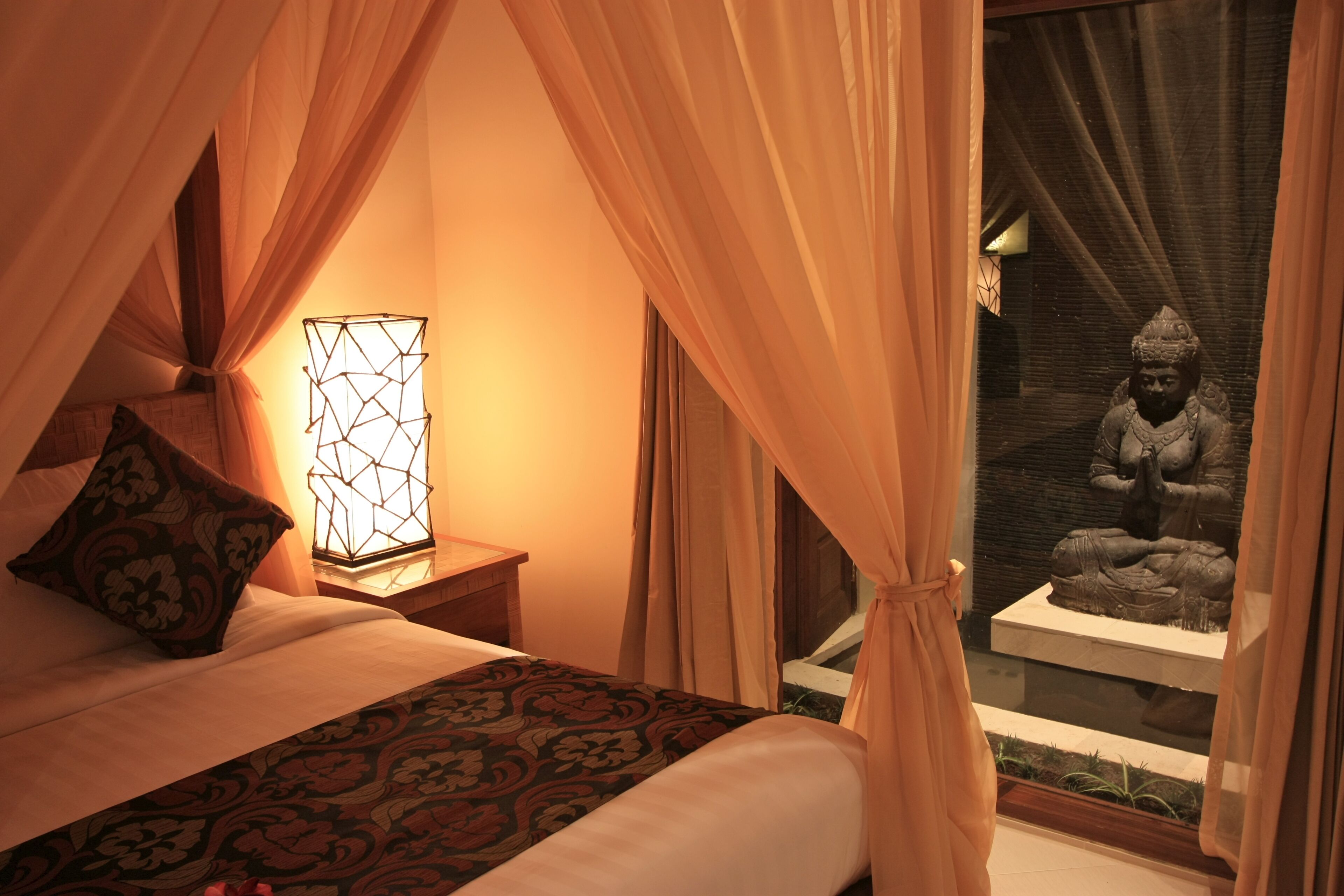 A bed with a patterned bedspread, a bedside lamp, and curtains.