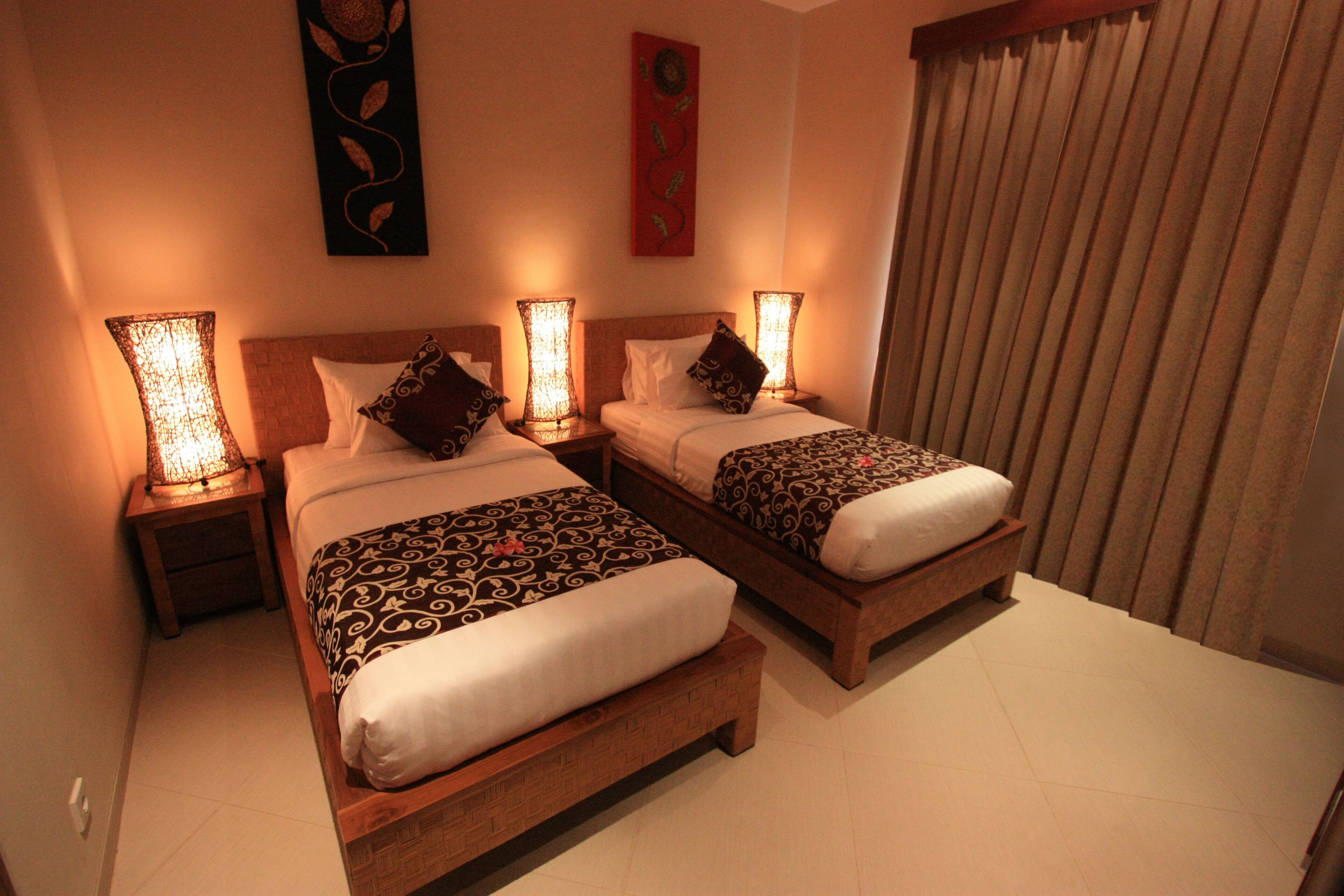 A hotel room with two wooden beds, each with patterned bedding and decorative pillows. There are bedside lamps on wooden nightstands.