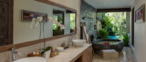 A modern bathroom with a large mirror, two sinks, a bathtub, and a view of a lush garden.